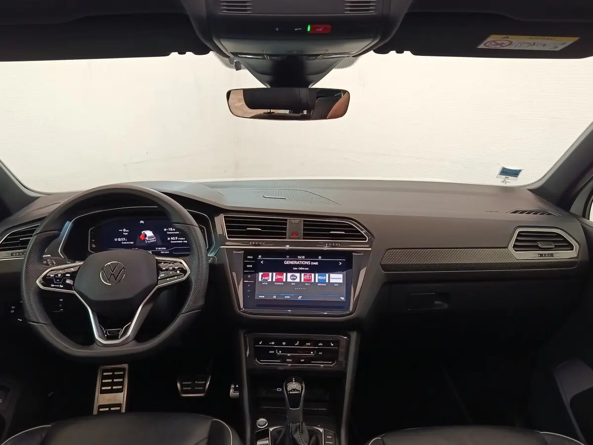 Vue intérieure frontale du tableau de bord noir du Volkswagen Tiguan 1.4 eHybrid 2023 avec écran tactile central et volant multifonctions.