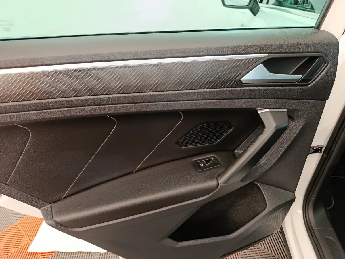Vue rapprochée de la porte avant gauche noire avec surpiqûres et insert décoratif du Volkswagen Tiguan blanc 2023.