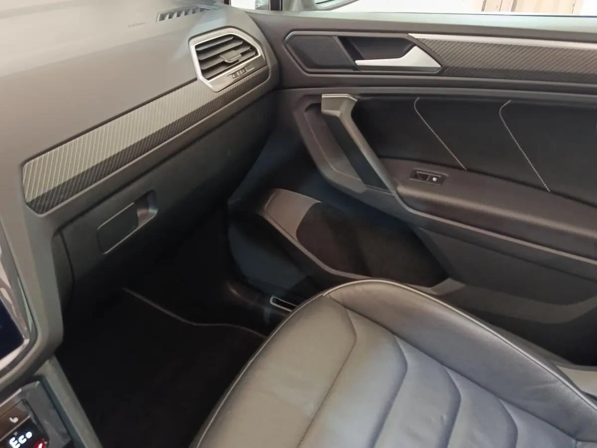 Vue intérieure côté passager du Volkswagen Tiguan 1.4 eHybrid 2023, avec siège cuir noir et garnitures carbone.