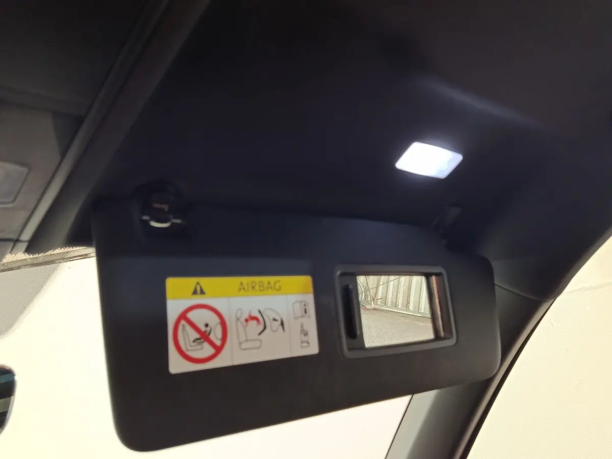 Pare-soleil intérieur noir avec miroir et avertissement airbag, vue en léger contre-plongée depuis l'habitacle.