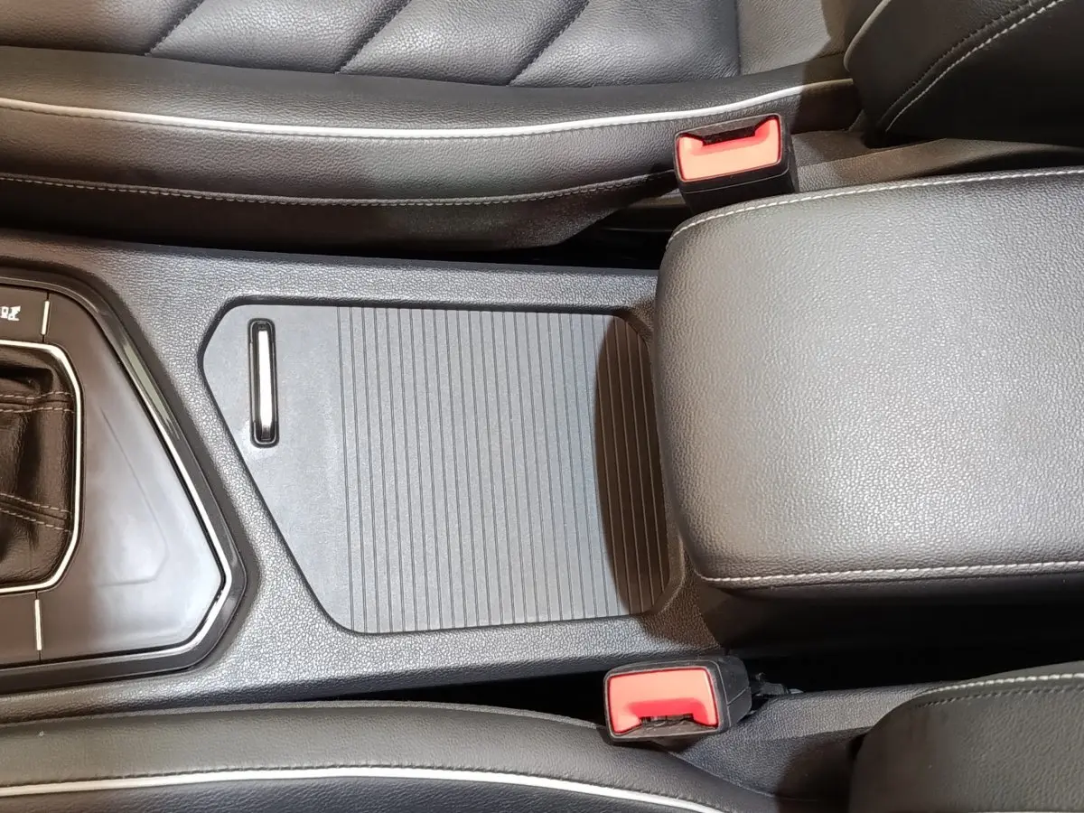 Vue rapprochée de la console centrale noire avec accoudoir et ceintures de sécurité rouges du Volkswagen Tiguan blanc 2023.
