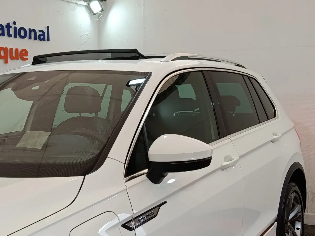 Vue 3/4 avant droit du Volkswagen Tiguan blanc hybride rechargeable avec badge eHybrid et toit ouvrant électrique visible.