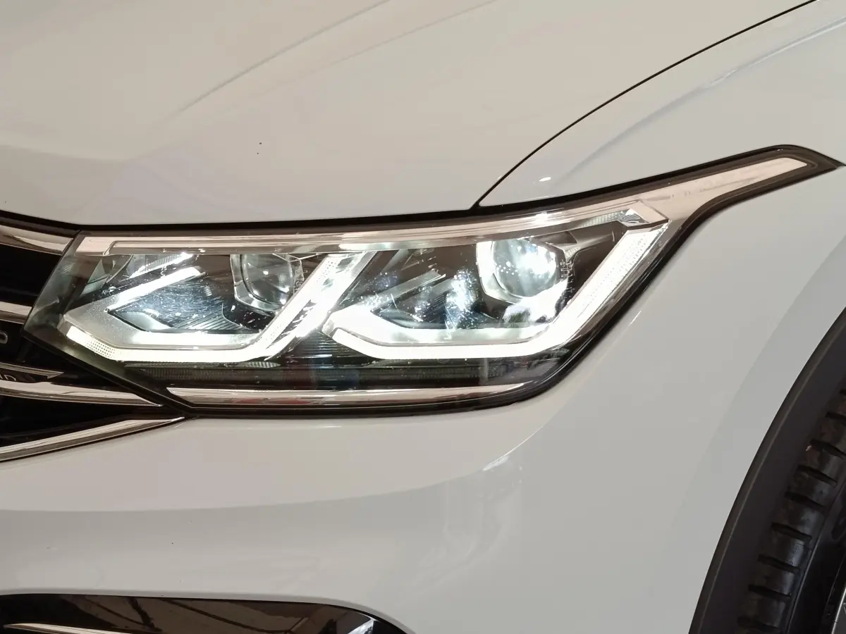 Gros plan sur le phare avant droit blanc du Volkswagen Tiguan 1.4 eHybrid 2023 avec signature lumineuse LED distinctive.