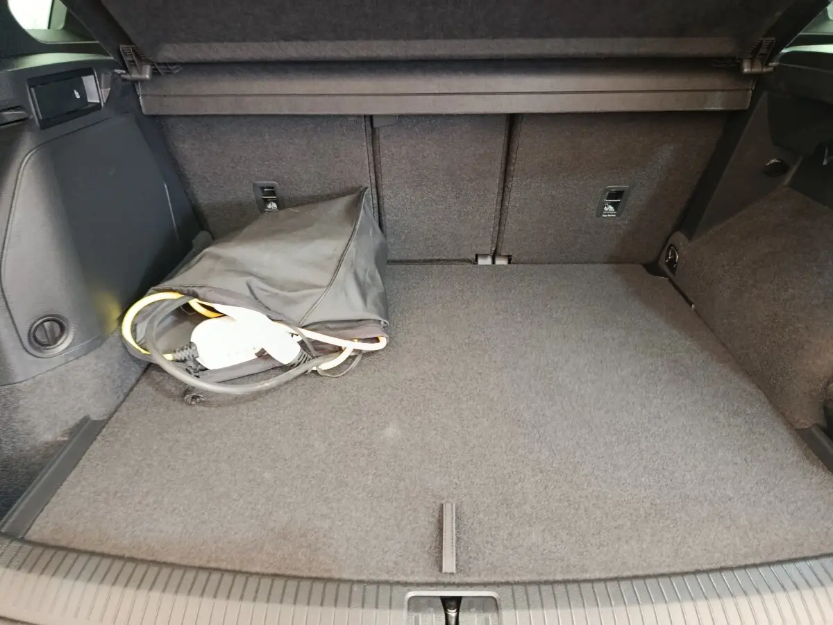 Vue du coffre arrière du Volkswagen Tiguan blanc 1.4 eHybrid 2023, avec câble de recharge et tapis gris.