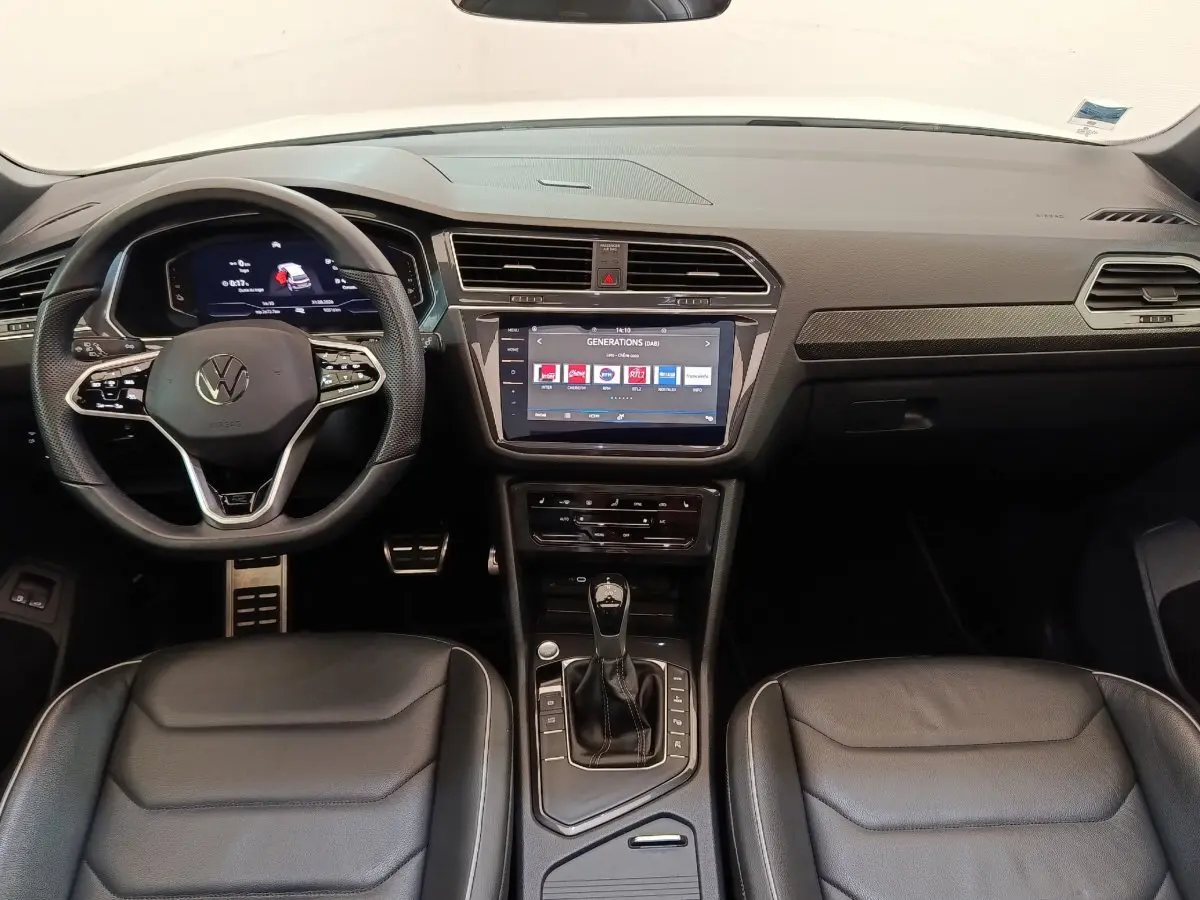 Vue intérieure avant du Volkswagen Tiguan blanc 2023, tableau de bord moderne avec écran tactile central et volant cuir multifonctions.