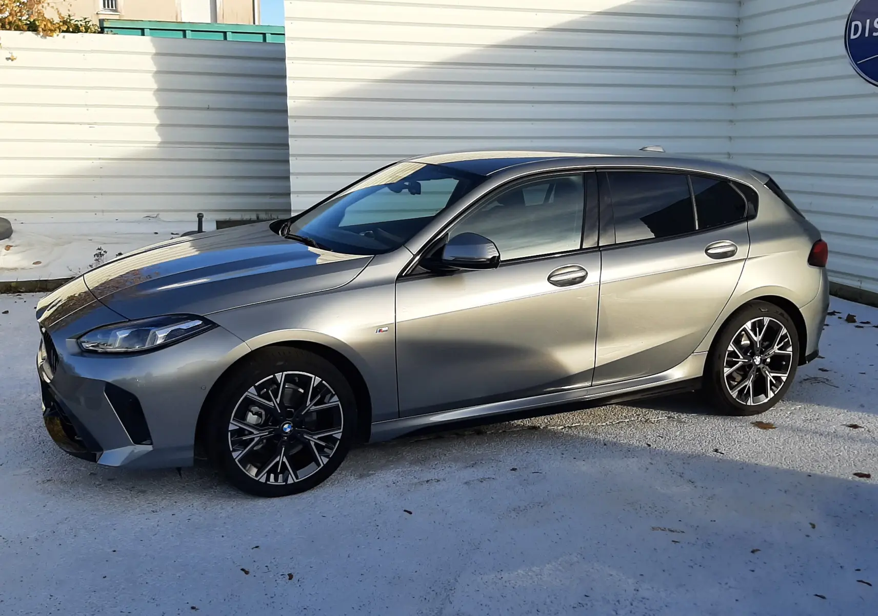 BMW Série 1 gris Skyscraper vue de profil côté gauche, avec jantes 18'' bicolores et finition M Sport Design.