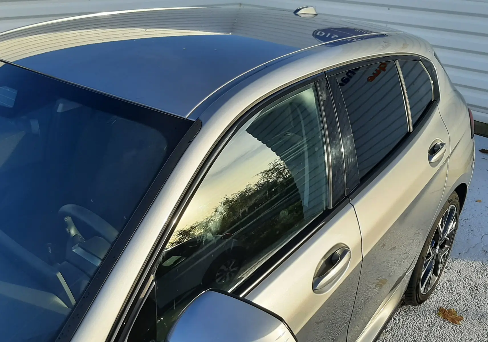 Vue plongeante sur le côté gauche d'une BMW Série 1 gris Skyscraper avec jantes 18'' bicolores et vitres teintées.