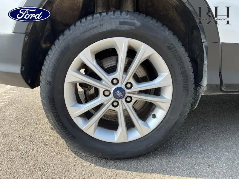 Gros plan sur la roue avant gauche du Ford Kuga blanc Glacier, mettant en valeur la jante alu et le pneu Bridgestone.