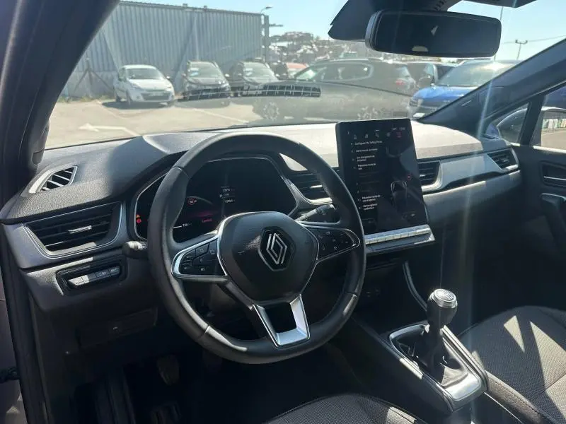 Vue intérieure avant du Renault Captur 2025 montrant le volant multifonction, écran tactile vertical et levier de vitesse manuel.