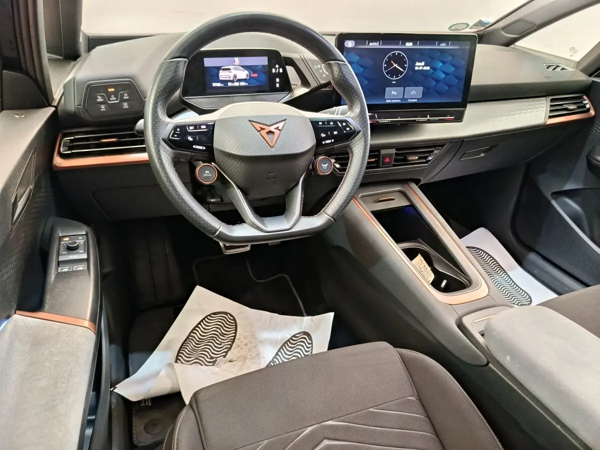 Vue intérieure avant du CUPRA Born 230ch gris foncé, avec volant multifonctions, écran tactile central et tableau de bord digital.