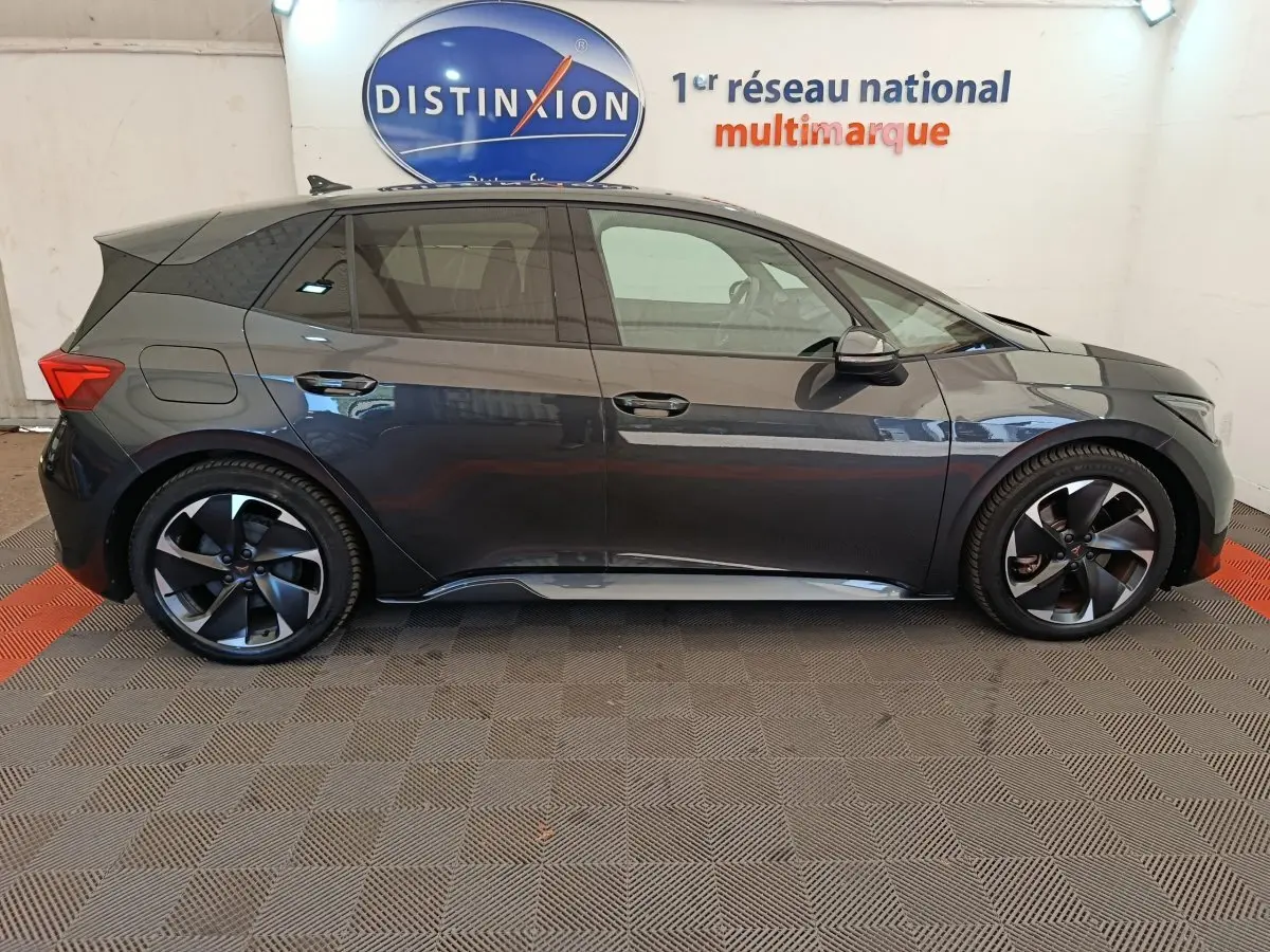 Vue de profil côté gauche d'une CUPRA BORN gris foncé 2023 avec jantes noires et toit noir dans un showroom.