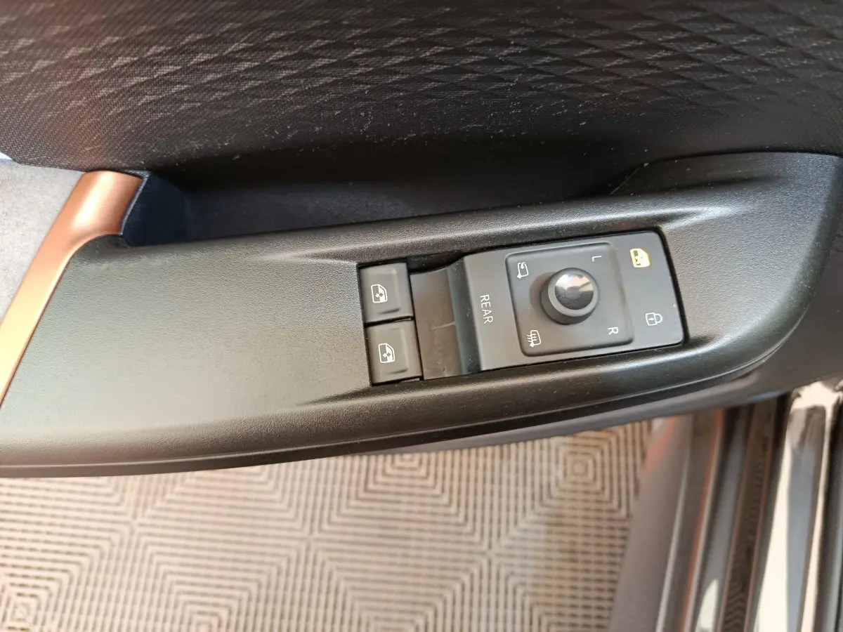 Gros plan sur les commandes de réglage des rétroviseurs et des vitres côté conducteur d'une CUPRA BORN gris foncé.