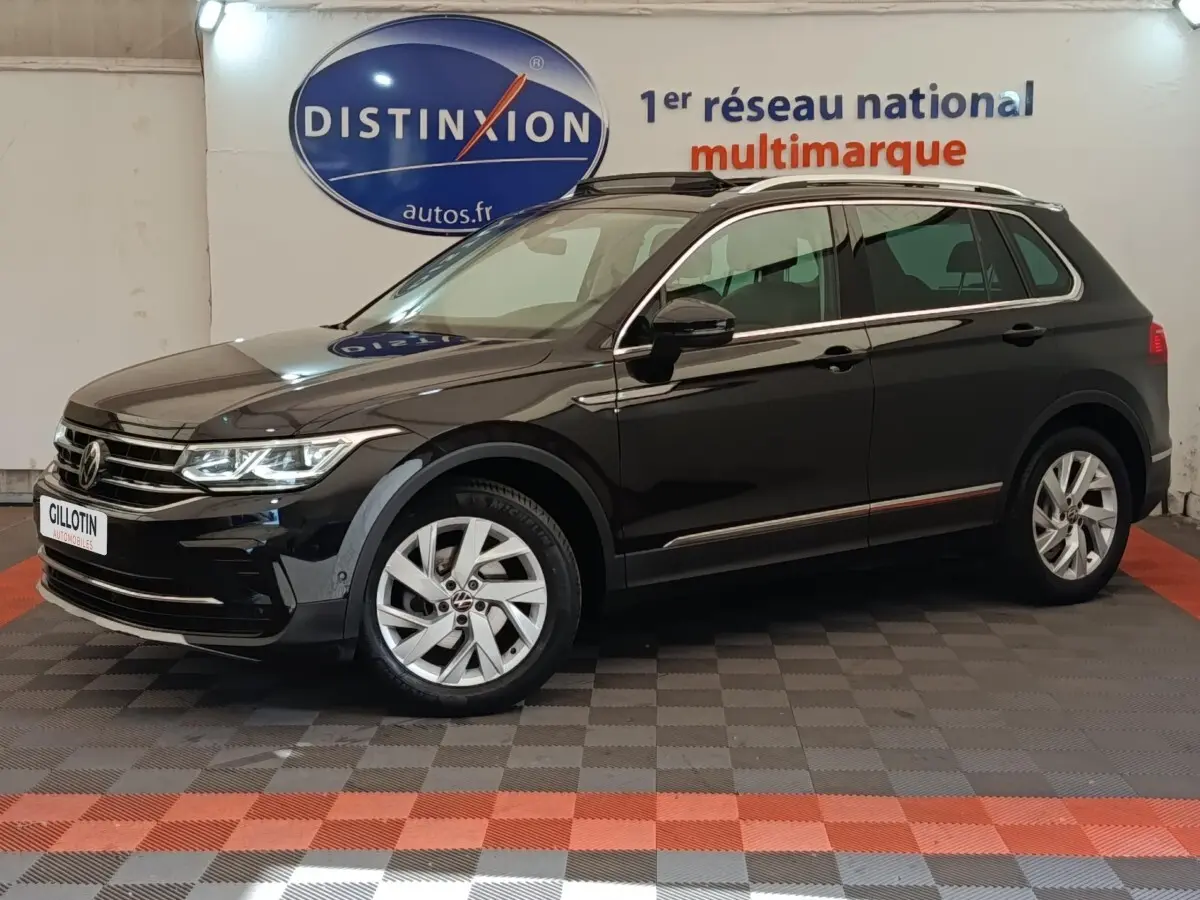 Volkswagen Tiguan noir 2021 en vue profil côté gauche, avec jantes alliage et barres de toit chromées visibles.