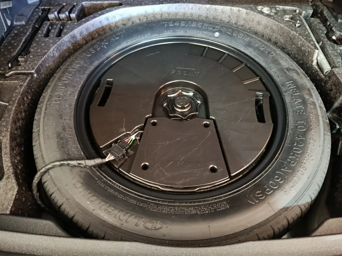 Gros plan sur la roue de secours dans le coffre du Volkswagen Tiguan noir, montrant le pneu et son boîtier central.