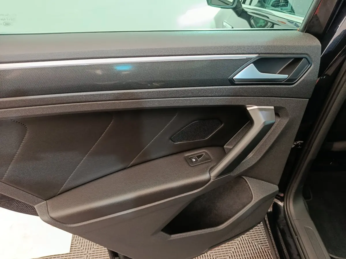 Gros plan sur la porte avant droite noire du Volkswagen Tiguan 2.0 TDI 150 DSG7 Elegance avec poignée argentée et bouton de vitre électrique.