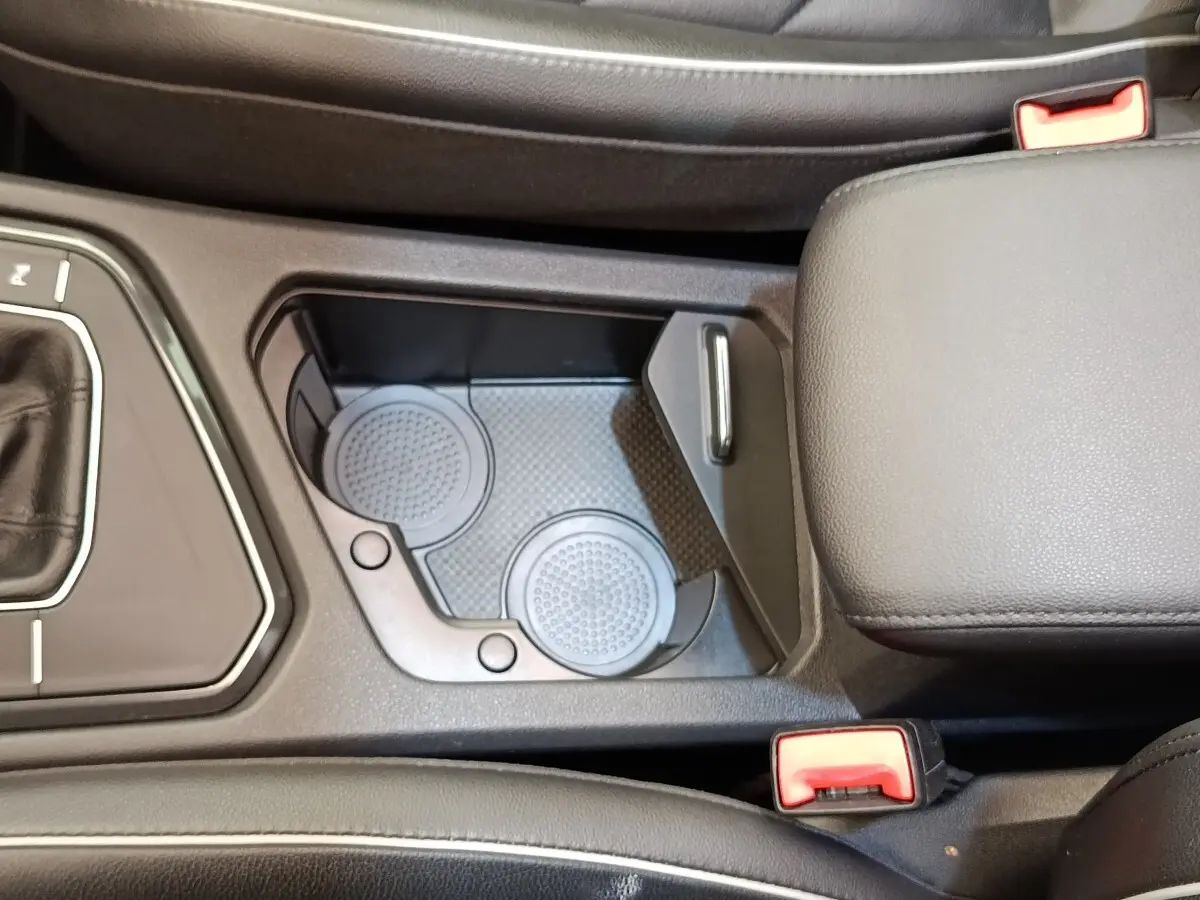 Vue rapprochée de la console centrale noire du Volkswagen Tiguan 2.0 TDI avec porte-gobelets et accoudoir cuir.