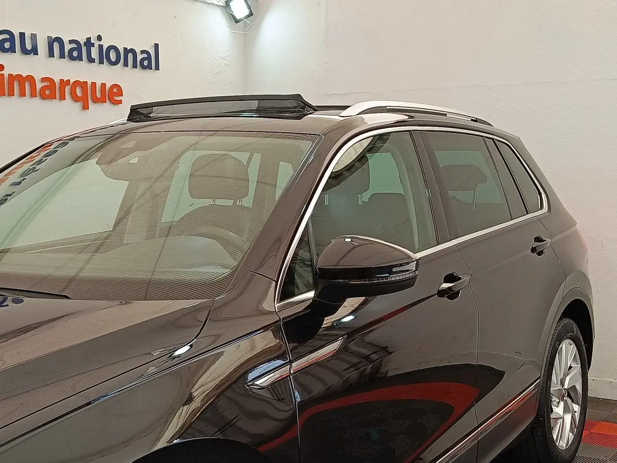 Vue 3/4 avant droit du Volkswagen Tiguan noir 2021, avec barres de toit chromées et rétroviseur droit à clignotant intégré.