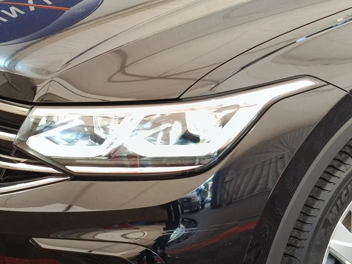 Gros plan sur le phare avant droit allumé d’un Volkswagen Tiguan noir, soulignant la calandre chromée et la carrosserie brillante.