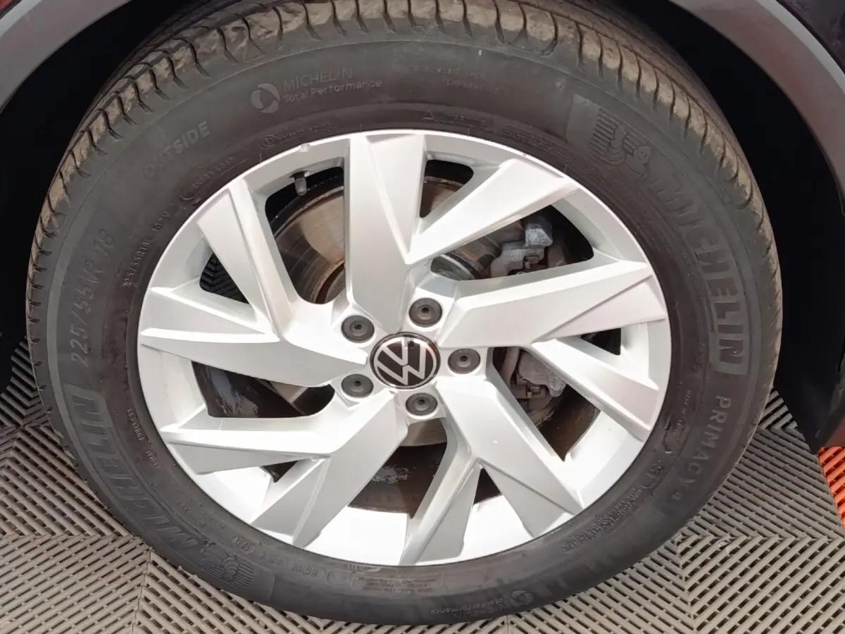 Gros plan sur la jante alliage argentée avec logo Volkswagen d’un Volkswagen Tiguan noir, pneu Michelin visible.
