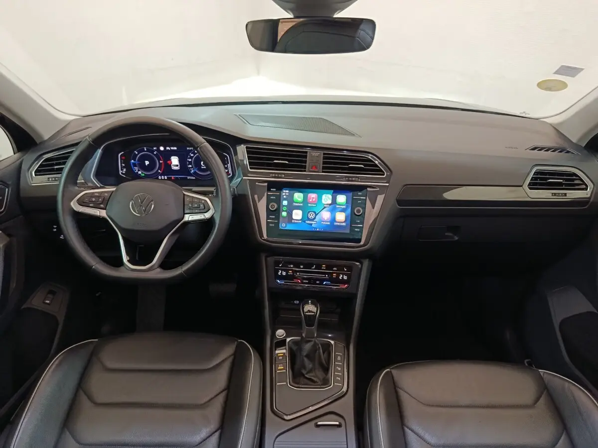 Vue intérieure du tableau de bord du Volkswagen Tiguan 2021, volant cuir multifonctions et écran tactile central allumé.