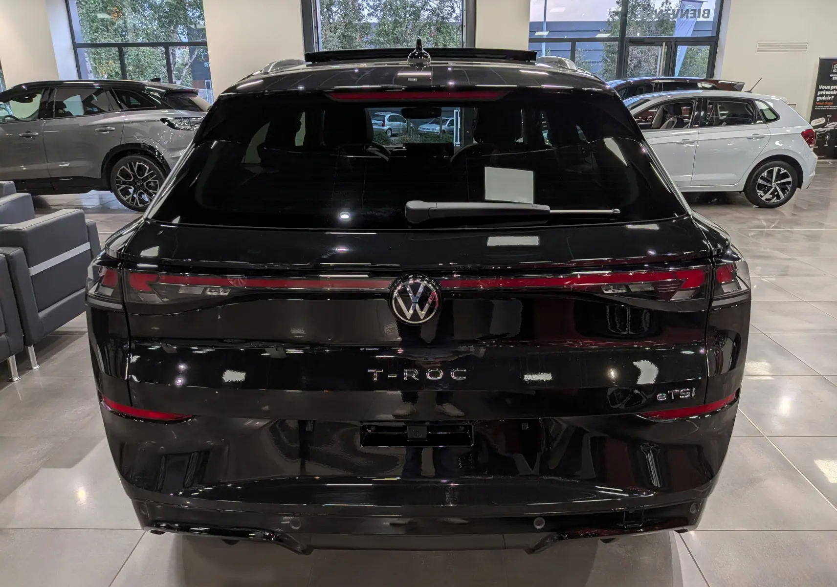 Vue arrière d’un Volkswagen T-Roc eTSI noir Ébène 2026 avec feux LED reliés et logo central lumineux dans un showroom.