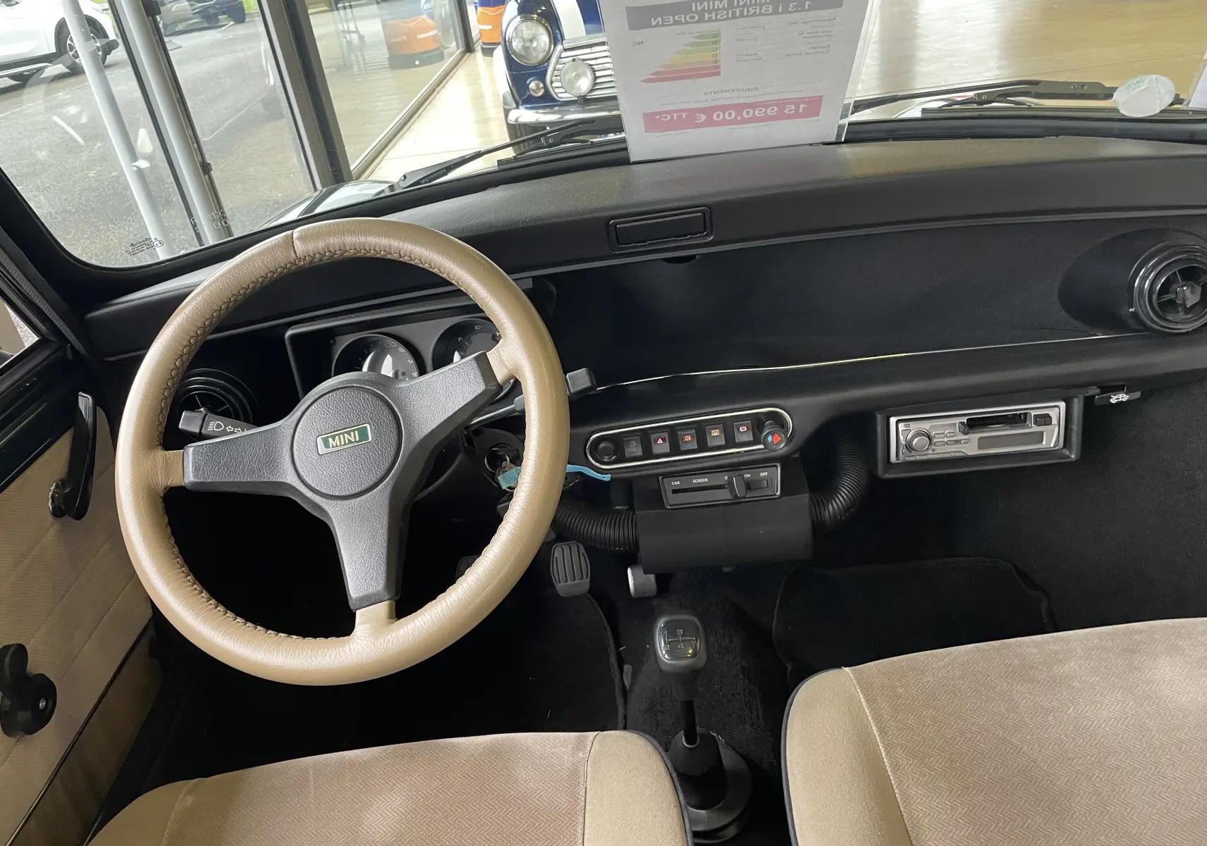 Intérieur de la MINI 1.3 i BRITISH OPEN 1995, vue du poste de conduite avec volant beige et tableau de bord noir simple.