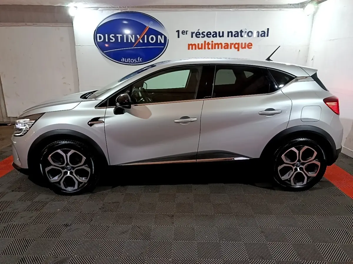 Profil droit d’un Renault Captur Intens E-Tech hybride rechargeable gris clair, avec jantes distinctives et vitres teintées.