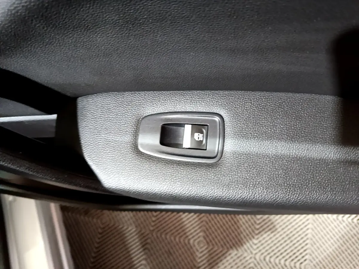 Gros plan sur le bouton de verrouillage des portes noir intégré à la garniture intérieure d'une Renault Captur gris clair.