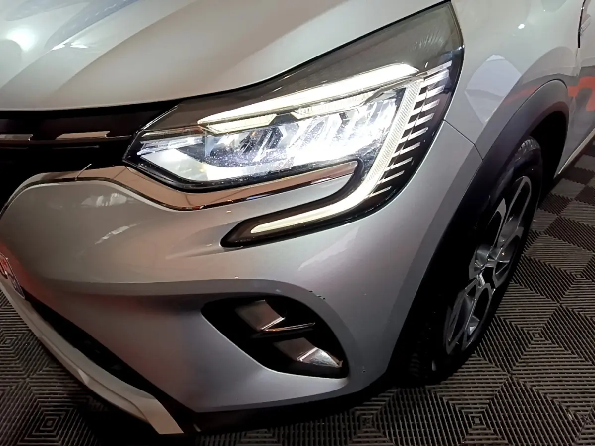 Gros plan sur le phare avant droit allumé d’un Renault Captur gris clair avec jante et partie de la calandre visibles.