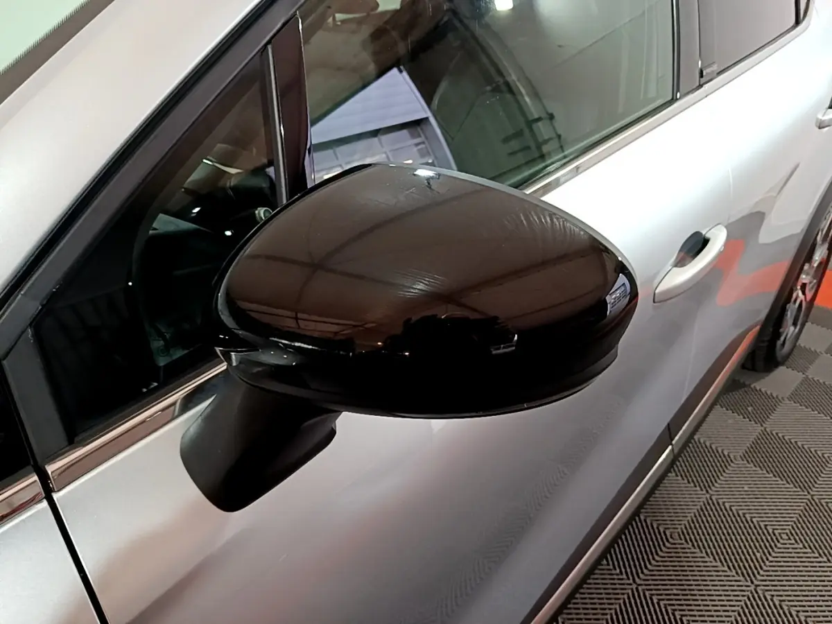 Gros plan sur le rétroviseur noir côté gauche d’un Renault Captur gris clair, vue partielle de la portière avant.