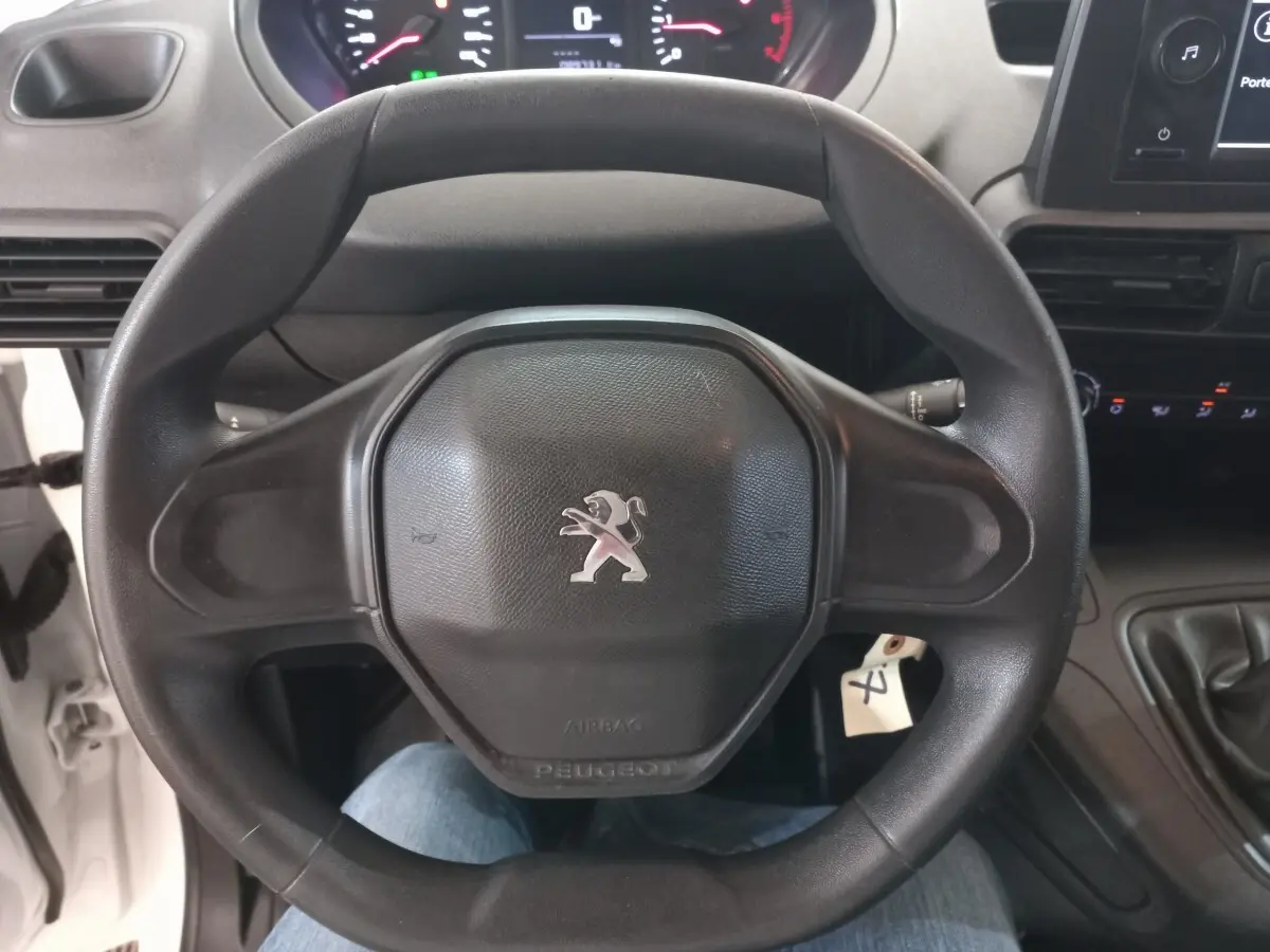 Vue rapprochée du volant noir avec logo Peugeot au centre dans l'habitacle d'un utilitaire blanc Peugeot Partner 2021.