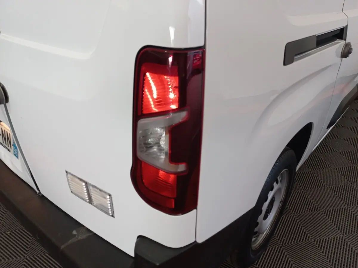 Vue arrière droite d’un utilitaire Peugeot Partner blanc avec feu arrière allumé et porte latérale coulissante.