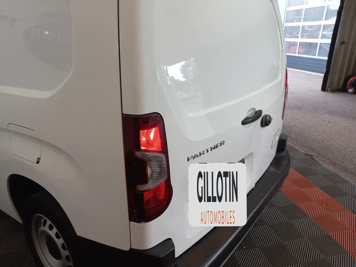 Vue arrière droite d’un Peugeot Partner blanc avec feux arrière allumés dans un garage.