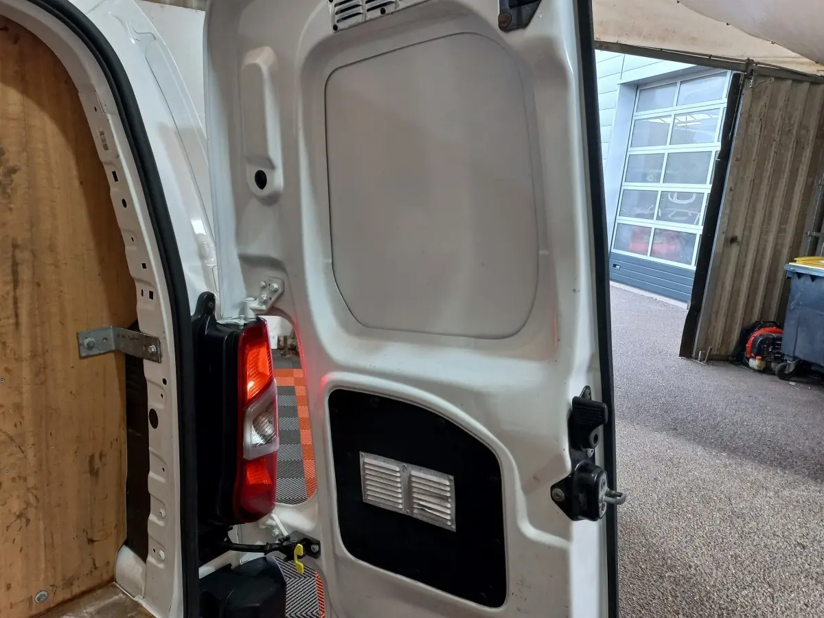 Vue rapprochée de la porte arrière droite ouverte d’un Peugeot Partner blanc, montrant le feu arrière et l’intérieur du véhicule.
