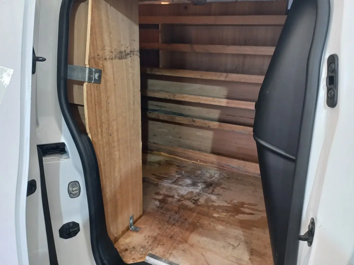 Vue intérieure du coffre arrière ouvert d’un utilitaire Peugeot Partner blanc, montrant la cloison et le plancher en bois.