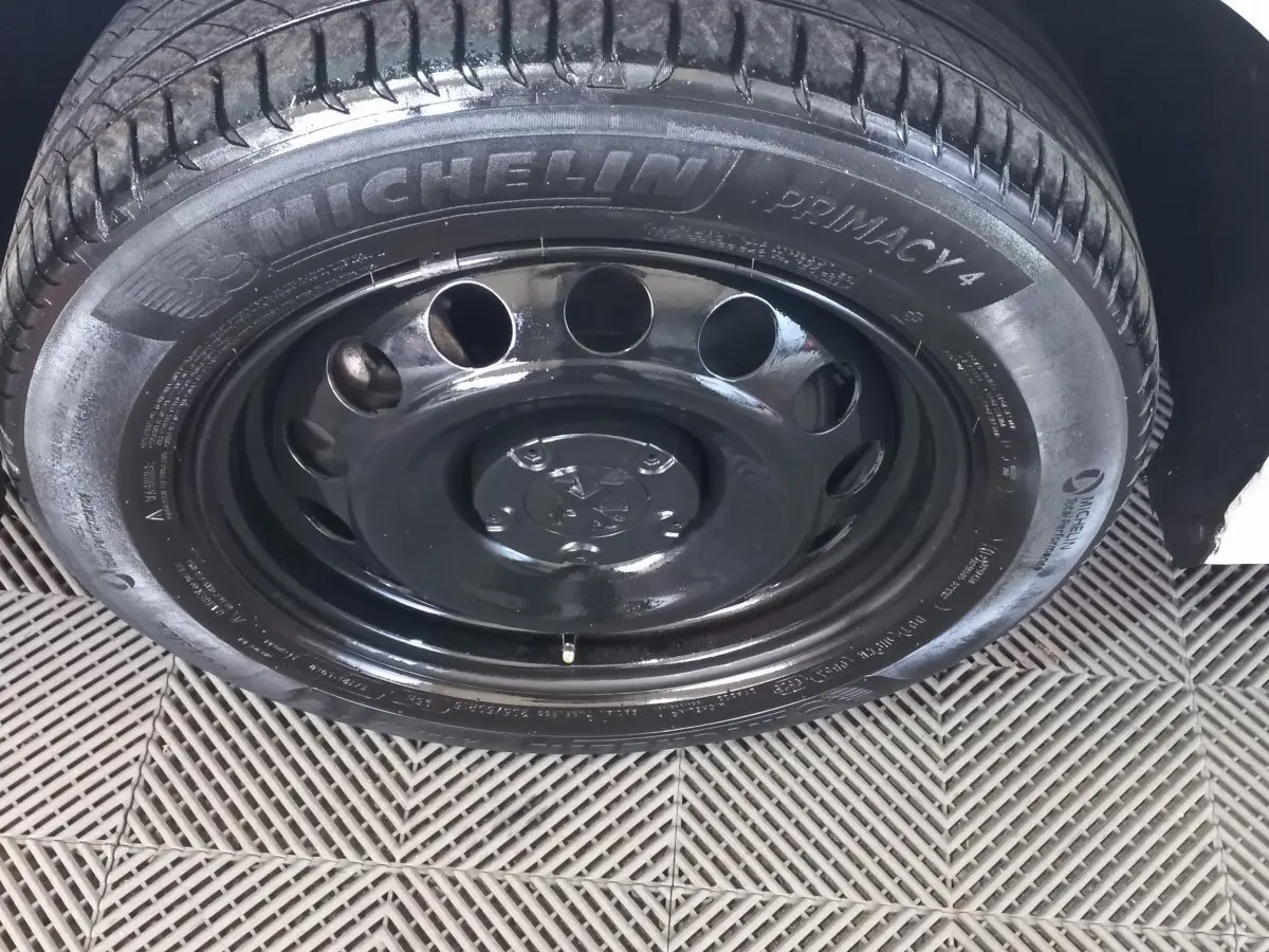 Gros plan sur la roue avant droite avec jante acier noire et pneu Michelin du Peugeot Partner blanc.