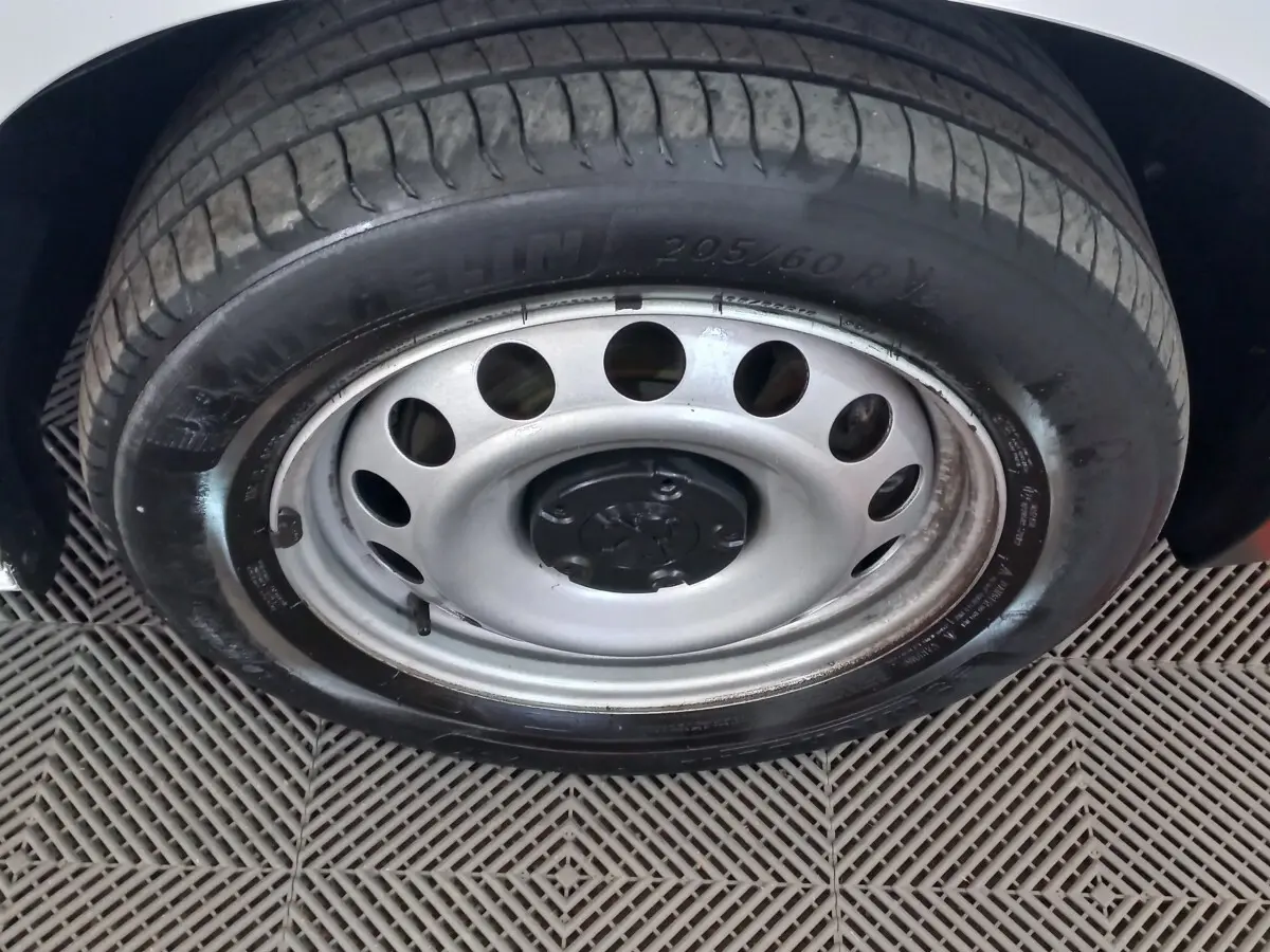 Gros plan sur la roue avant droite avec jante acier et pneu Michelin du Peugeot Partner blanc 2021.