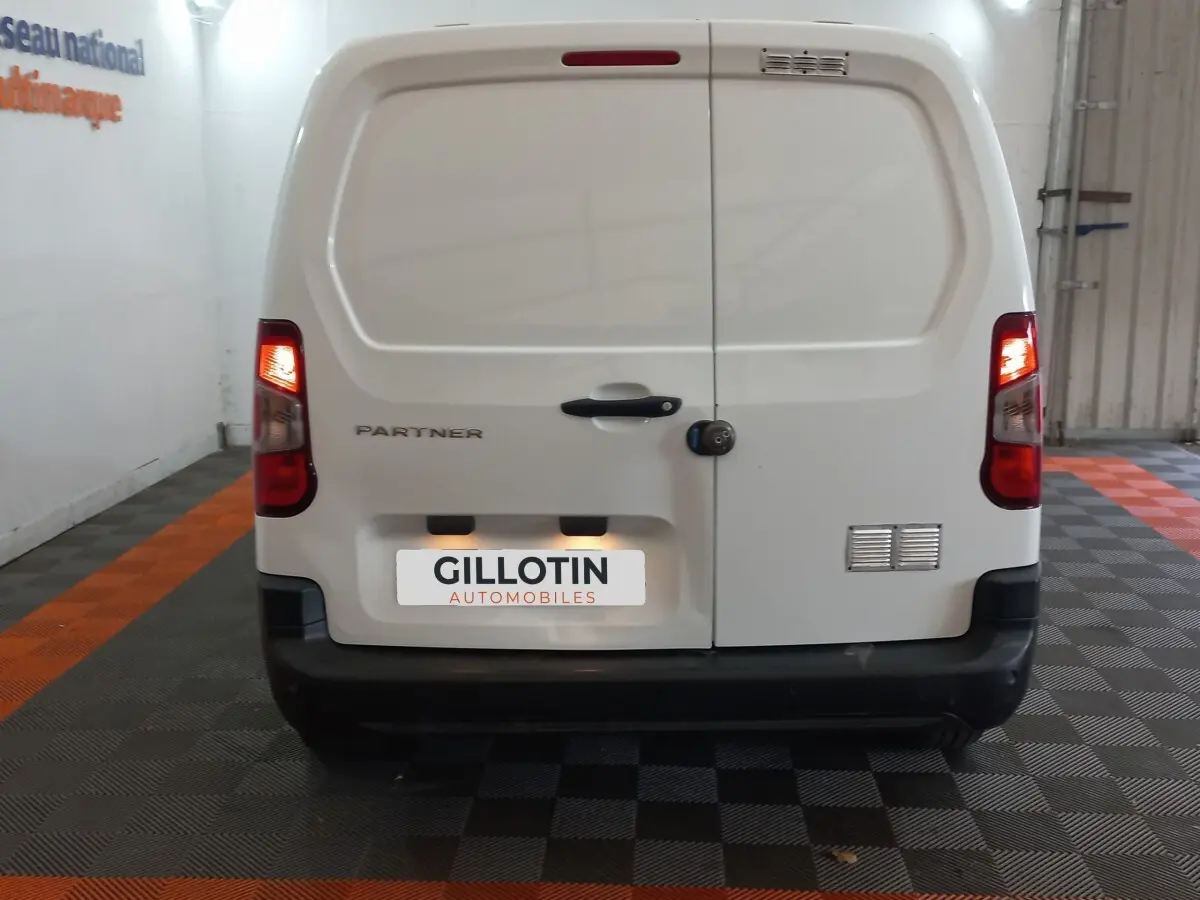 Vue arrière d’un utilitaire Peugeot Partner blanc avec feux arrière allumés dans un garage.