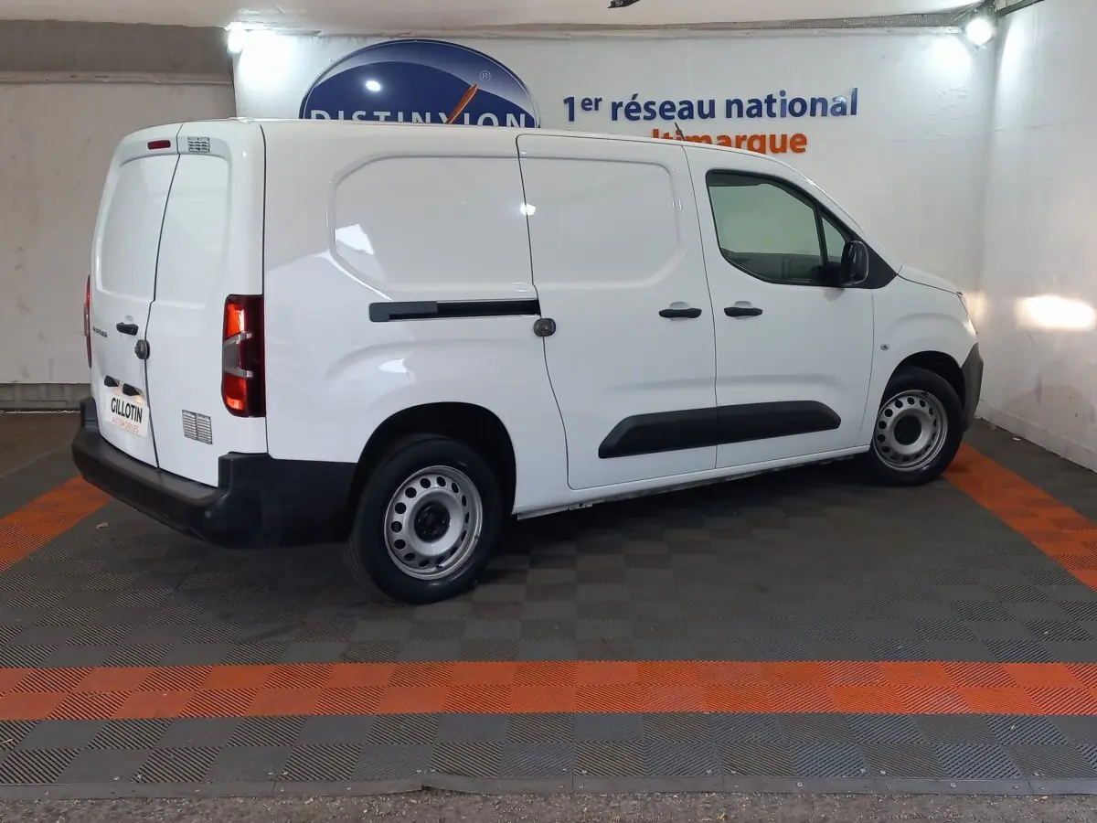 Vue 3/4 arrière droite d’un utilitaire Peugeot Partner blanc avec portes latérales et arrière pleines, en intérieur.