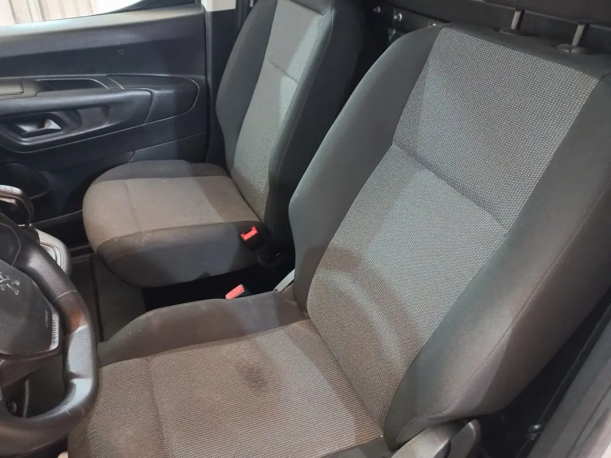 Vue intérieure côté conducteur du Peugeot Partner 2021, sièges tissu gris et noir avec volant partiellement visible.