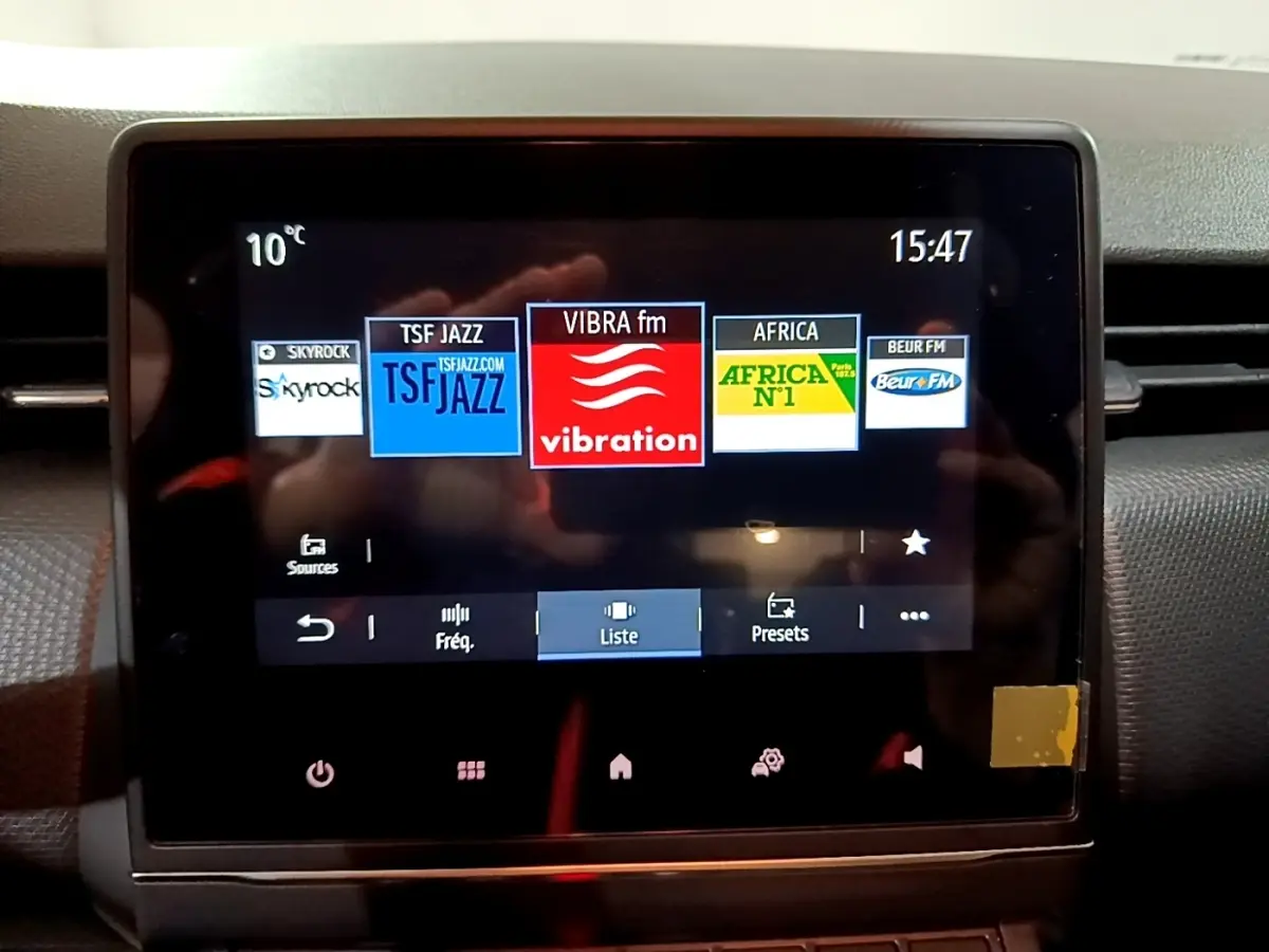 Écran tactile central de la Renault Clio gris clair, affichant les stations radio avec interface moderne.