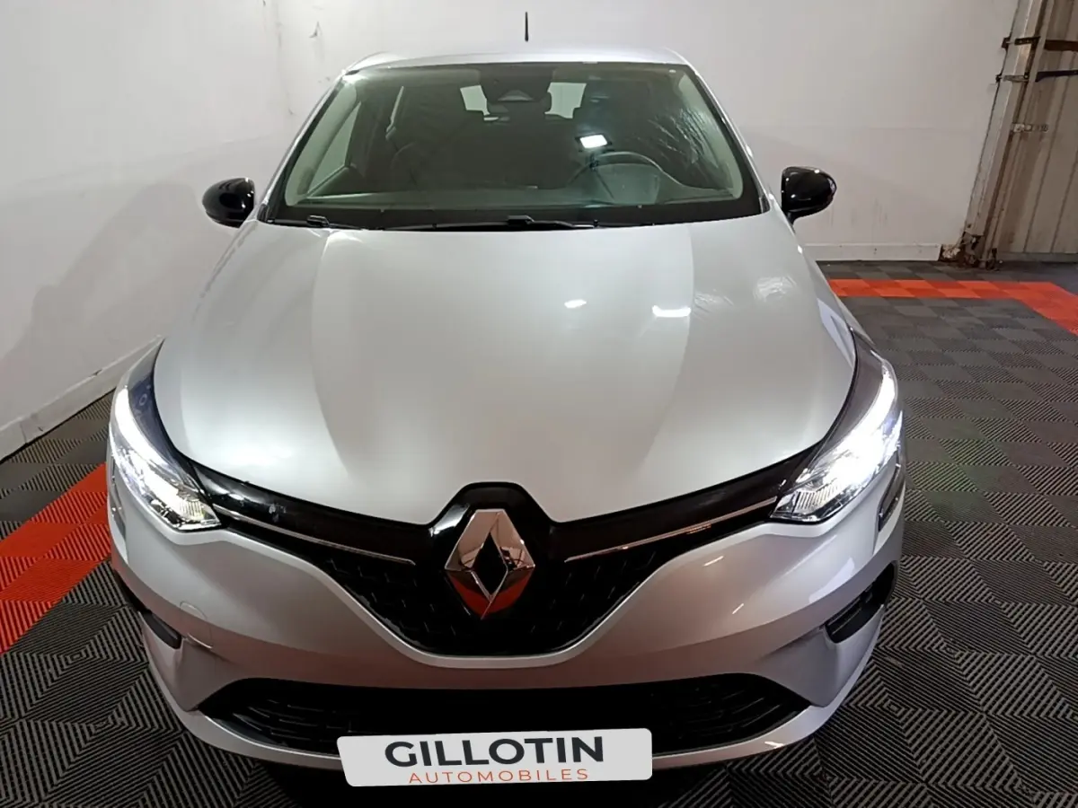 Vue avant d'une Renault Clio gris clair 2023 avec phares LED allumés dans un garage.
