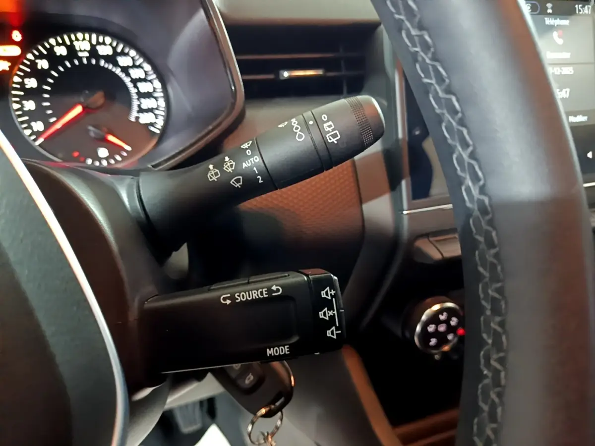 Gros plan sur la colonne de direction et commandes au volant cuir d'une Renault Clio gris clair, tableau de bord partiellement visible.