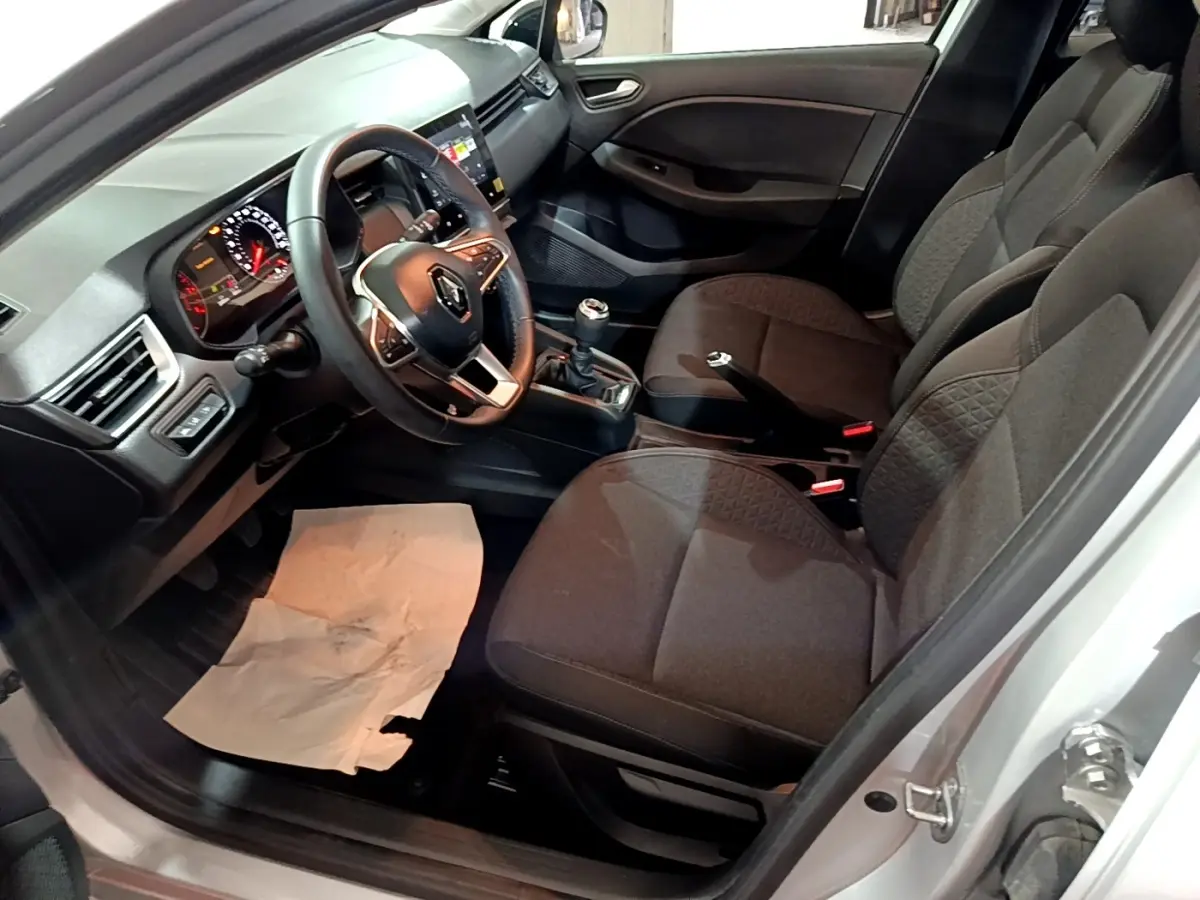 Vue intérieure côté conducteur de la Renault Clio gris clair 2023, volant cuir, tableau de bord avec écran tactile et boîte manuelle.