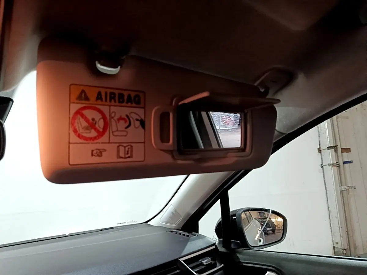 Vue intérieure côté conducteur de la Renault Clio gris clair 2023, avec pare-soleil ouvert et miroir de courtoisie visible.