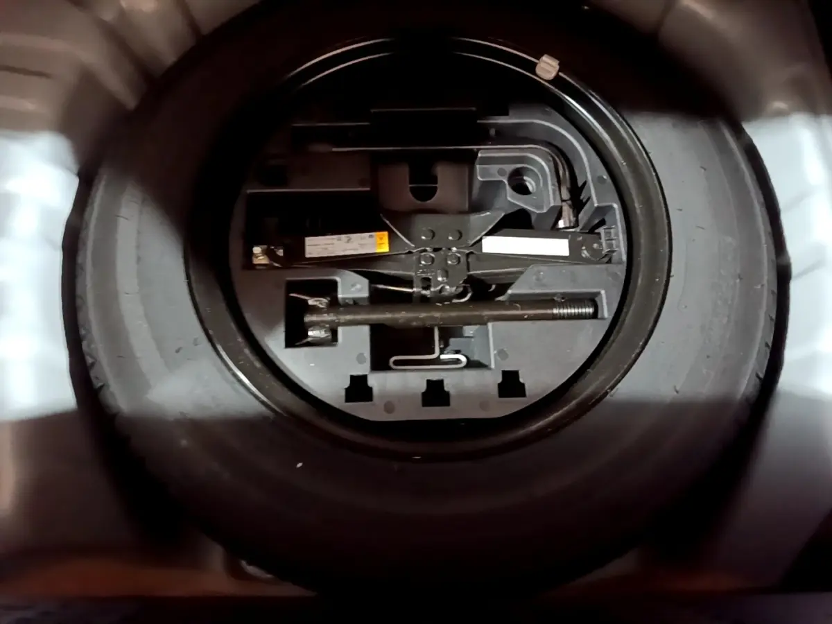 Gros plan sur la roue de secours noire et son outillage dans le coffre d'une Renault Clio gris clair 2023.