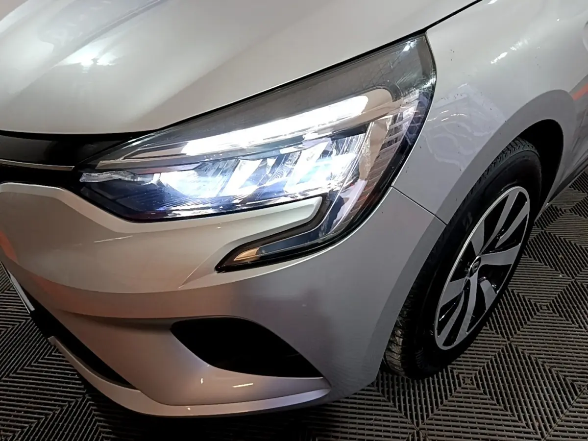 Gros plan sur l'avant droit gris clair de la Renault Clio 2023, mettant en valeur le phare LED et la jante design.