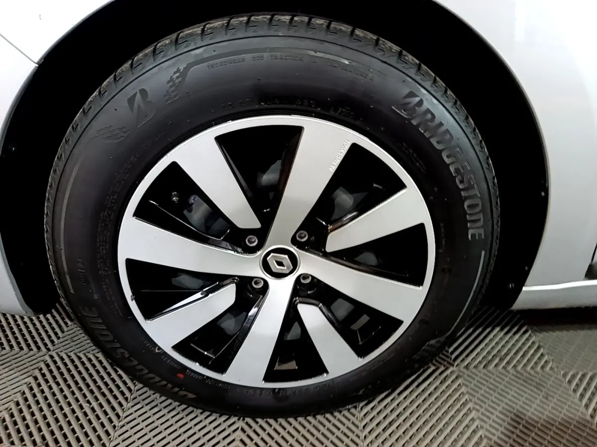 Gros plan sur la roue avant gauche d'une Renault Clio gris clair avec jante alliage bicolore et logo Renault central.