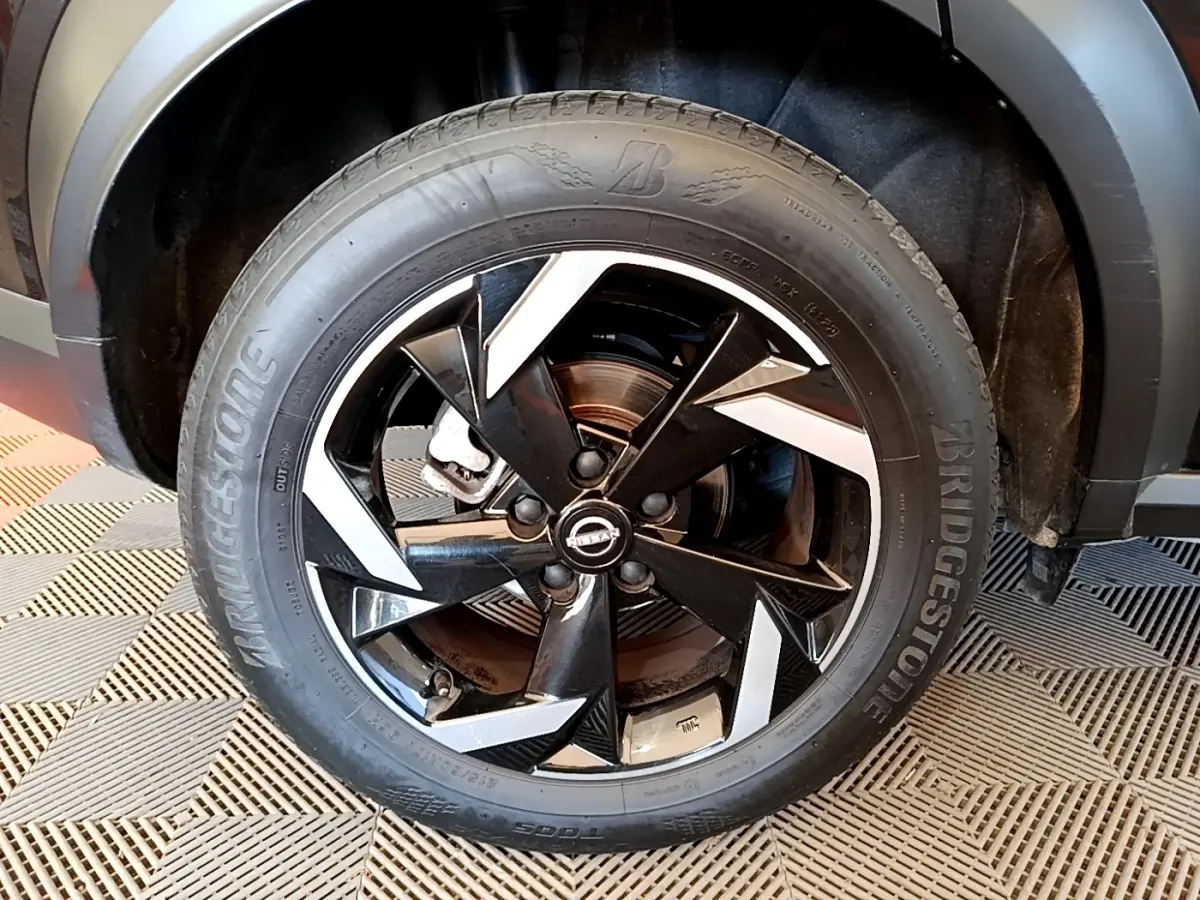 Gros plan sur la roue avant droite noire du Nissan Juke 2022 avec jante alliage noire et détails argentés.