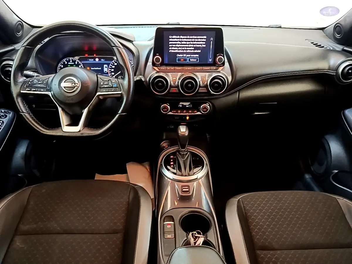 Vue intérieure avant du Nissan Juke noir 2022, tableau de bord avec écran tactile central et volant multifonctions.